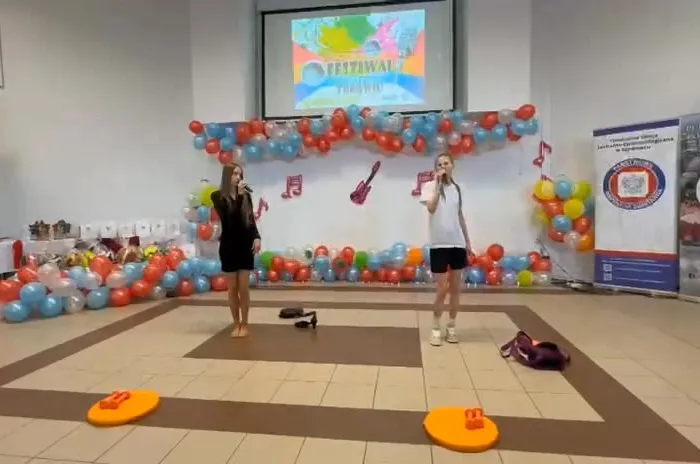 Dwie uczennice śpiewają na tle balonów i banerów
